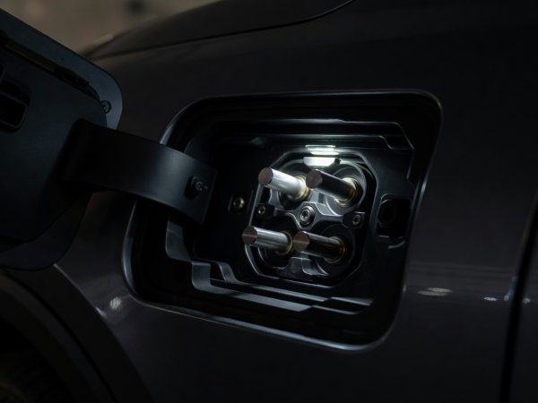 Close-up of an illuminated electric vehicle charge port inlet showing AC upper pins and DC high-current lower pins
